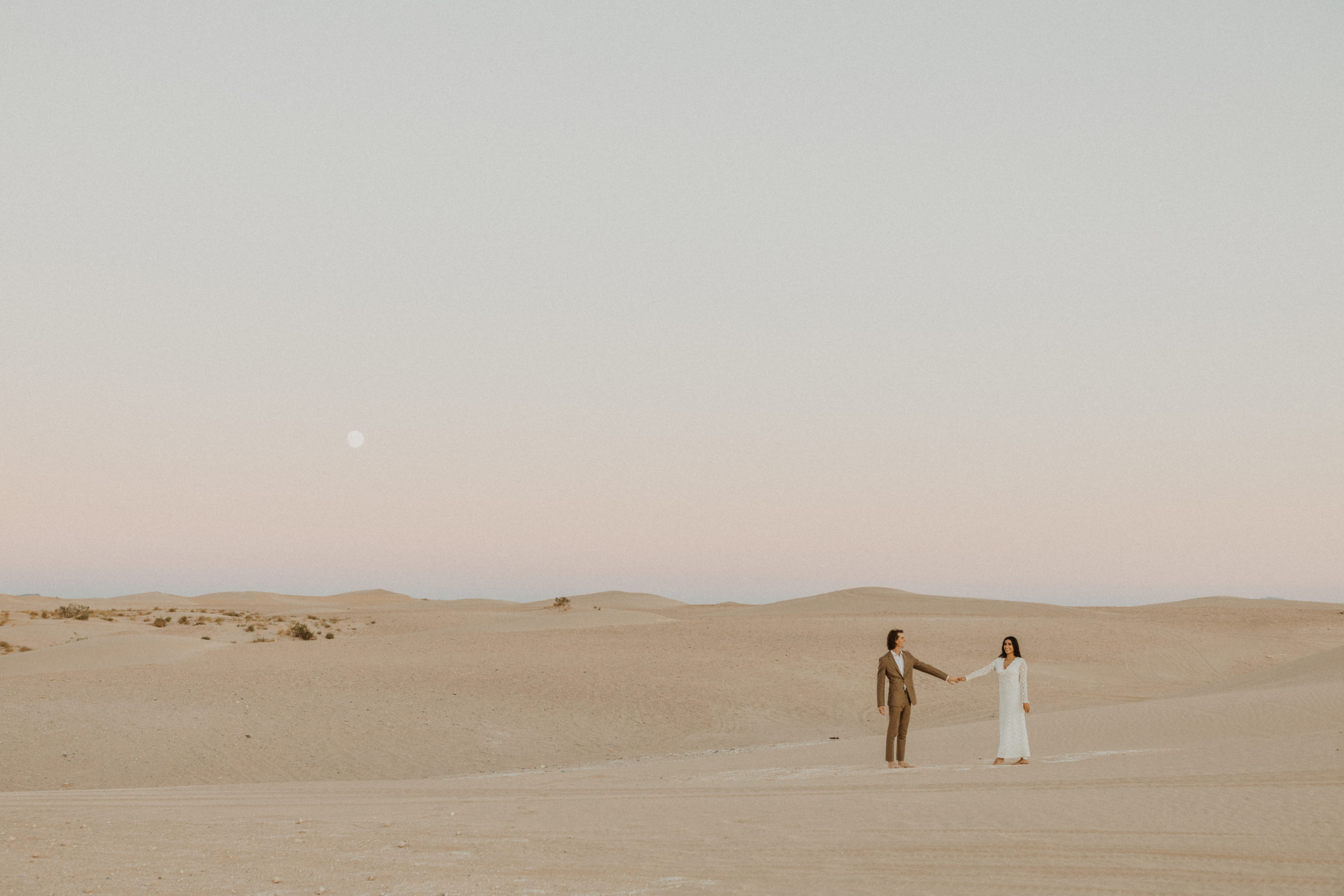 bride and groom standing in sand dunes